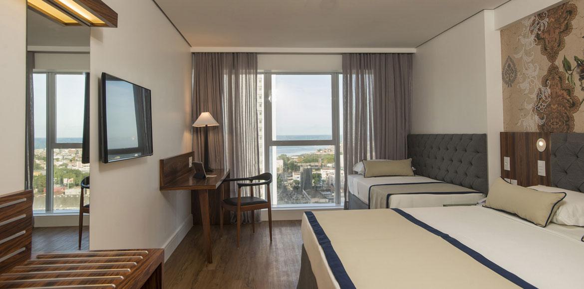 Hotel Luzeiros Ресифи Экстерьер фото The photo shows a modern hotel room. It features two beds with a simple design, one larger and one smaller. There's a large window with sheer curtains, allowing natural light to fill the space and offering a view of the outside. A wooden desk and cha
